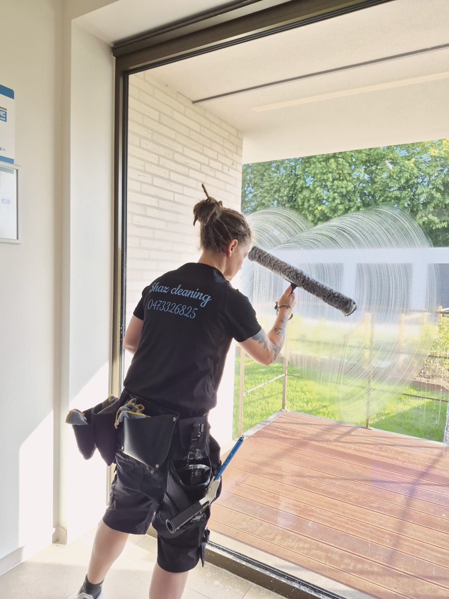 Medewerker van Shaz Cleaning poetst een raam in bedrijfsshirt